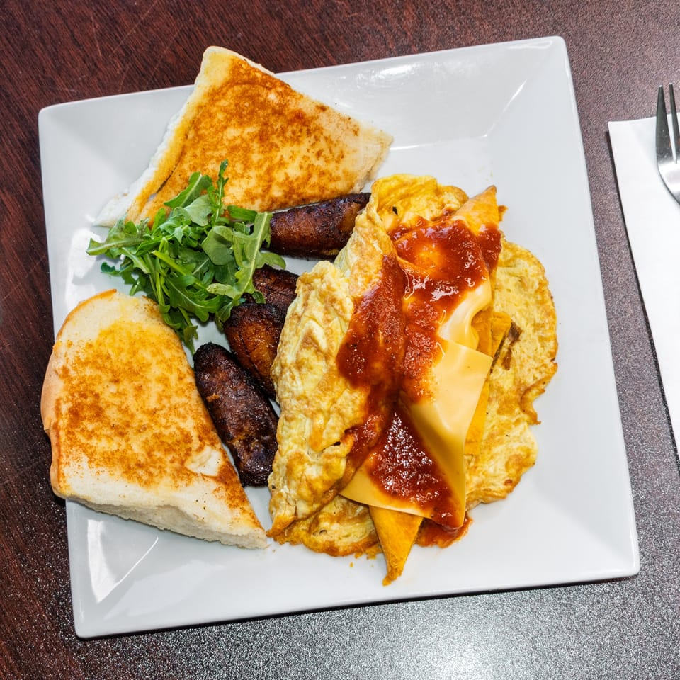 A breakfast plate with scrambled eggs, cheese, salsa, fried plantains, and toasted bread.