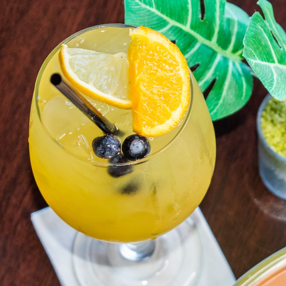A refreshing yellow drink with lemon, orange, and blueberries, served in a stemmed glass.