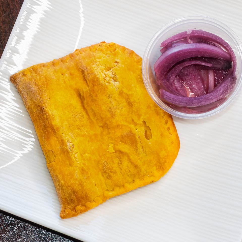 A golden-brown pastry with a side of pickled red onions in a clear container on a white plate.