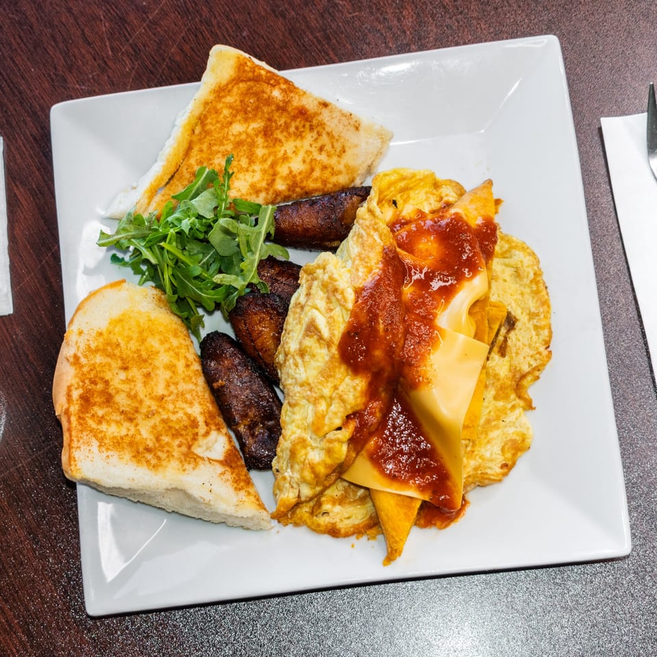 A breakfast plate with scrambled eggs, cheese, salsa, fried plantains, and toasted bread.