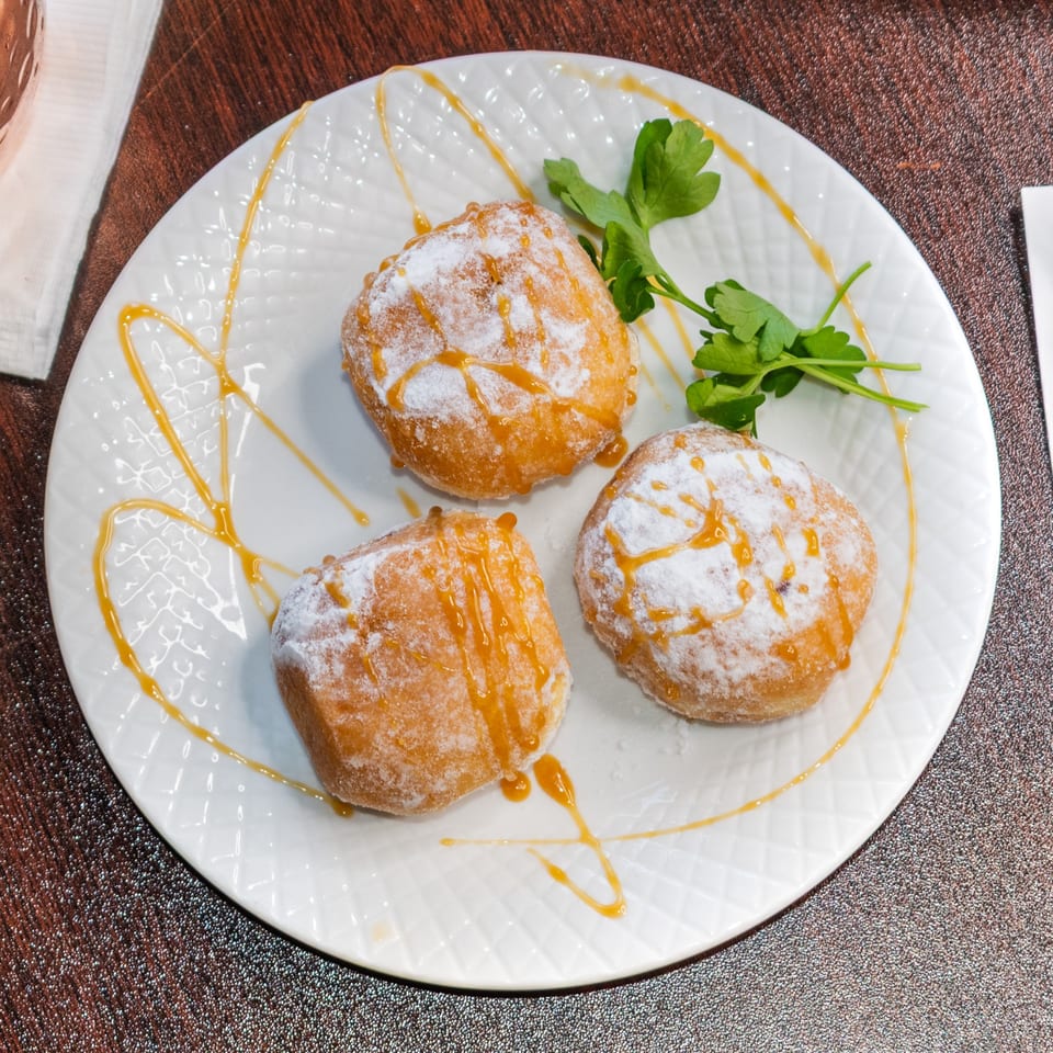 Three golden-brown donuts, powdered sugar, and caramel drizzle on a white plate with parsley garnish.