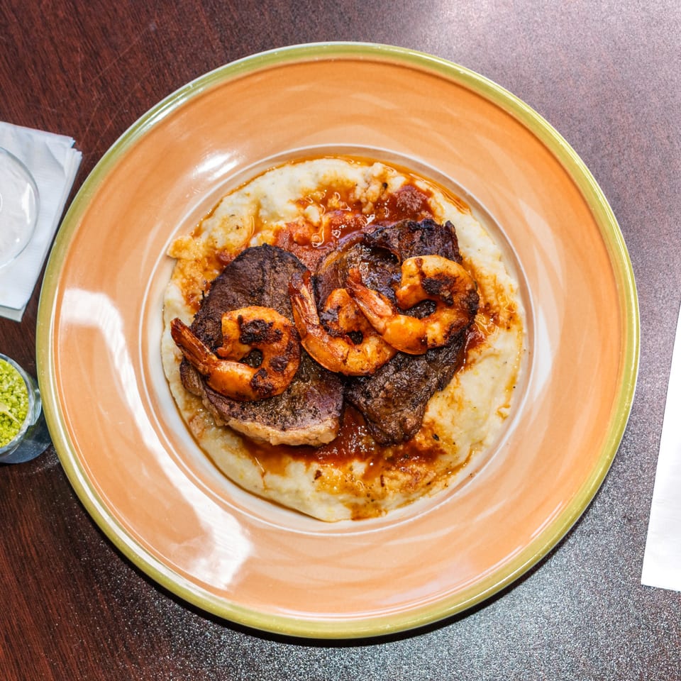Ore A Love Story's steak and shrimp dish with mashed potatoes and sauce on an orange plate.