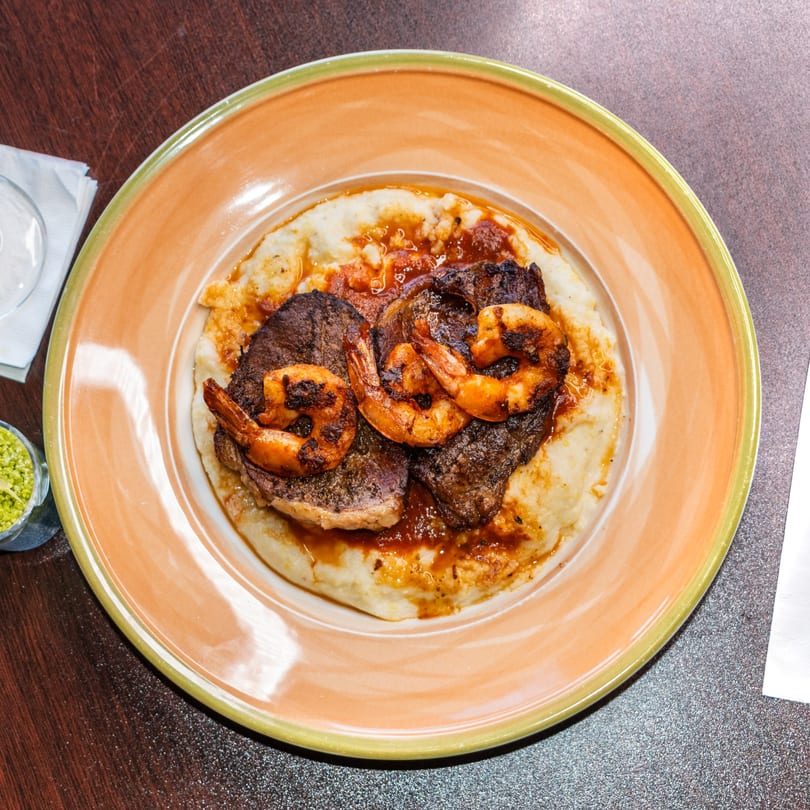 Ore A Love Story's steak and shrimp dish with mashed potatoes and sauce on an orange plate.