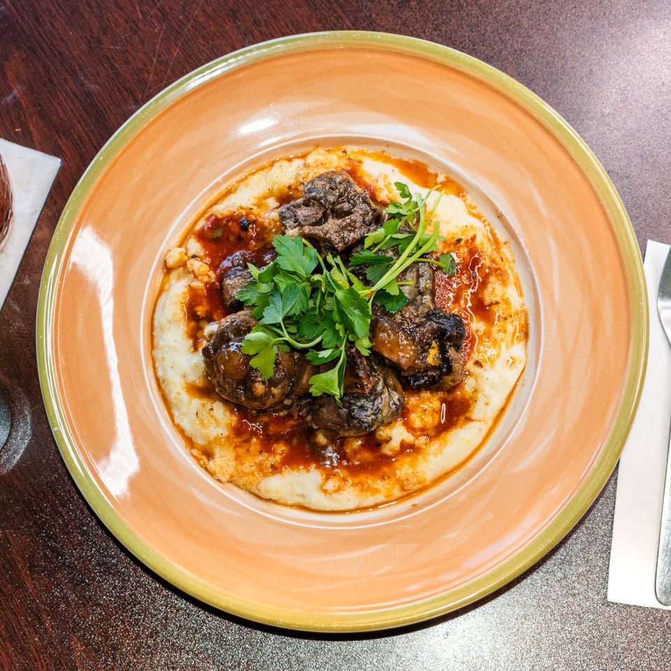 Braised short ribs with creamy grits and a rich sauce, garnished with fresh parsley on an orange plate.